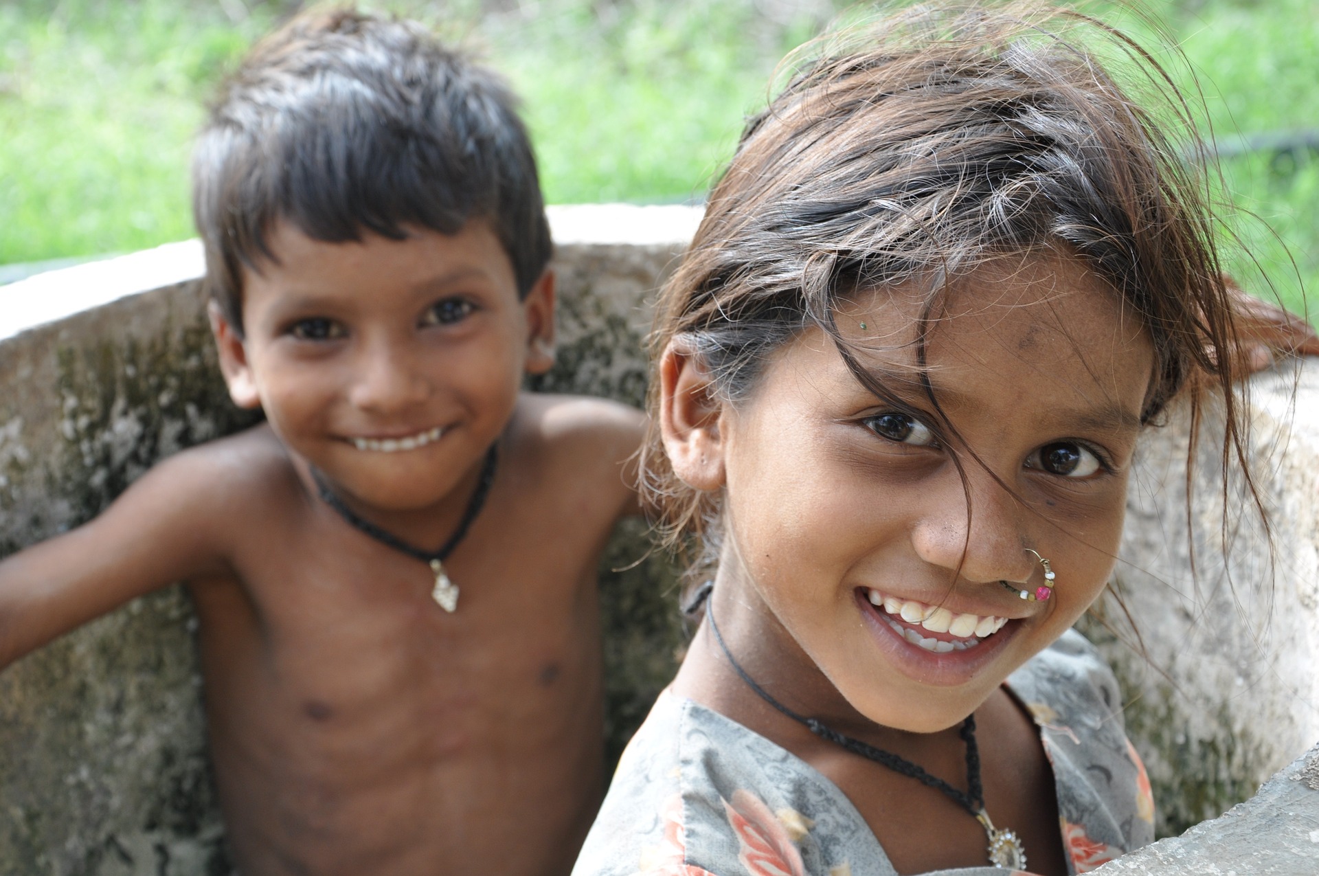 Zwei fröhliche Kinder, ein Junge im Hintergrund und ein Mädchen im Vordergrund, die indianisch-amerikanischer Abstammung sind, lachen in die Kamera, während sie in einem Betonrohr sitzen.
