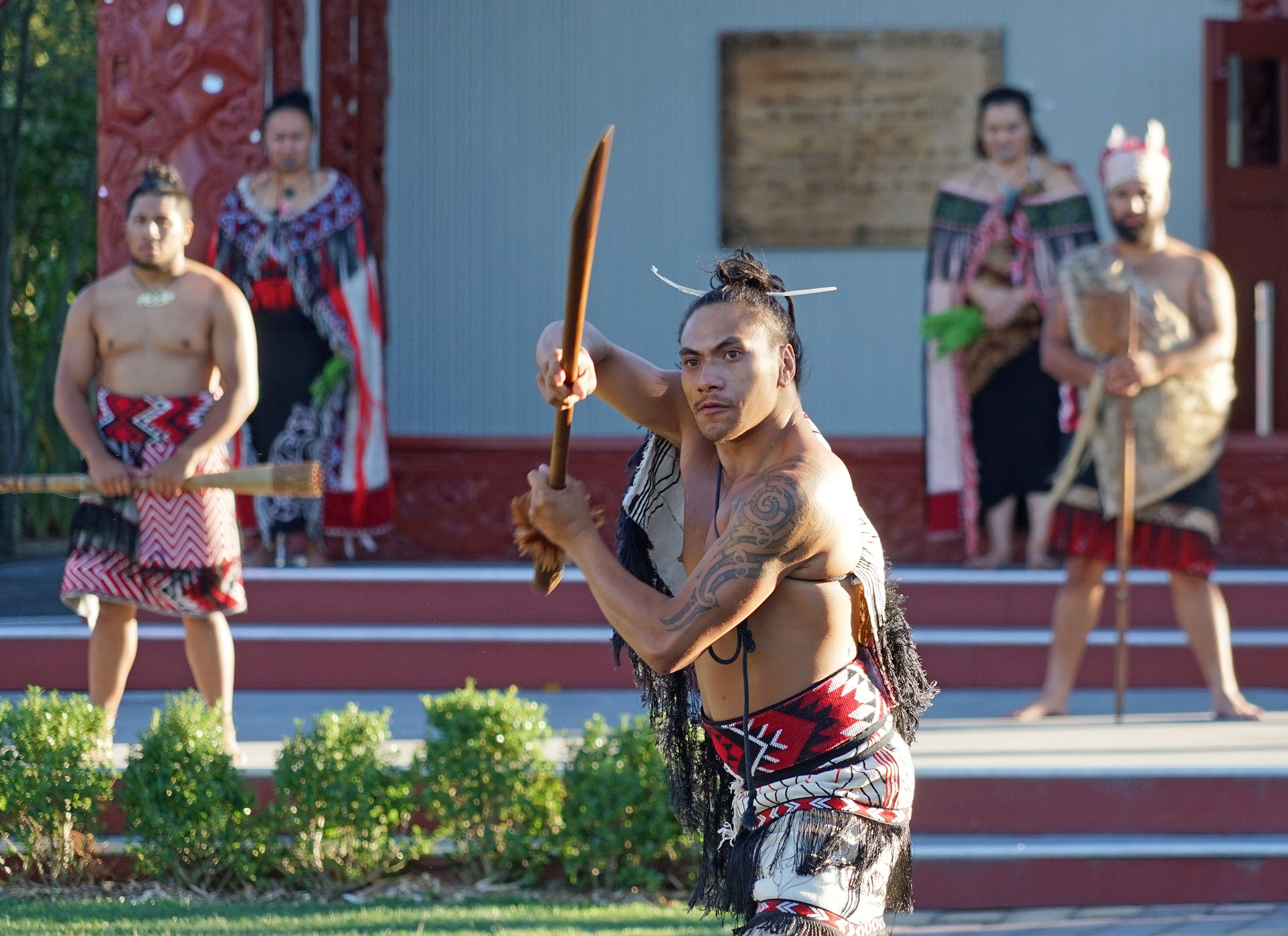 Ein Maori Krieger zeigt sich im Showkampf in Großaufnahme mit einem Schwert. Im Hintergrund sind weitere Maori Krieger zu sehen.