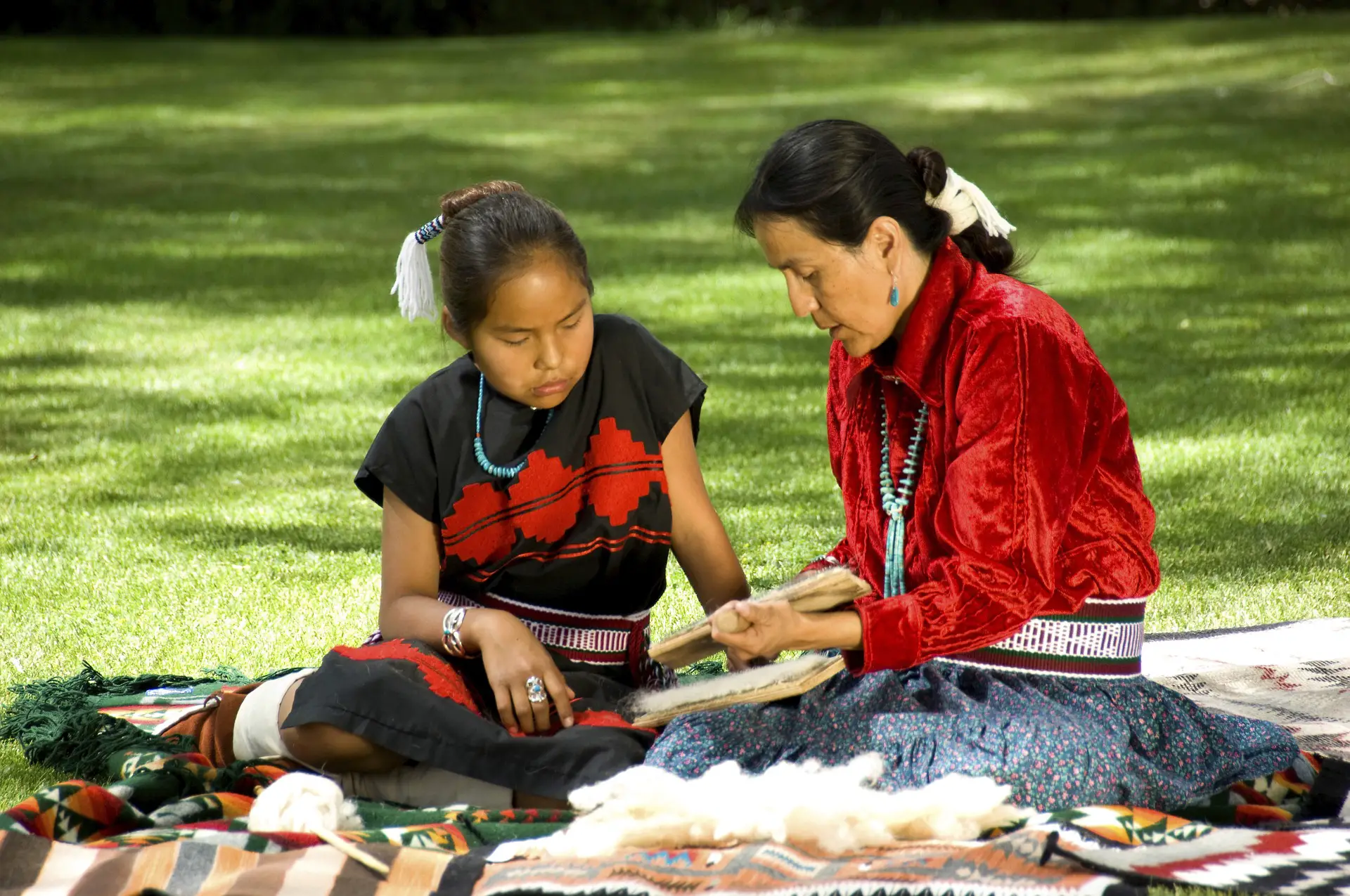 Eine Navajo-Mutter sitzt mit ihrer Tochter auf einer Decke im Park und teilt ihr Wissen über ihre Kultur.